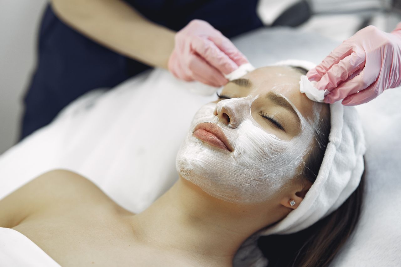 ours-journey From above anonymous medical specialist in uniform and gloves wiping cream mask off face of relaxed woman during skincare procedure in modern studio