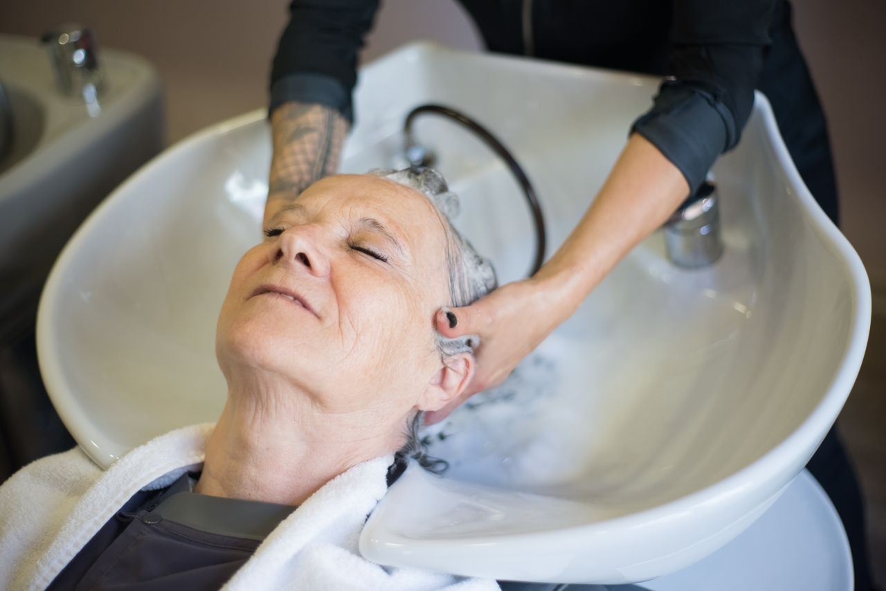 services-01 Senior woman relaxing during a hair wash at a salon. The hairstylist gently massages her hair in an inviting, serene setting.